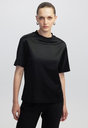 Camiseta negra de manga corta, hecha de tejido suave, con cuello redondo y un corte holgado. Combinada con pantalones negros, diseño minimalista.