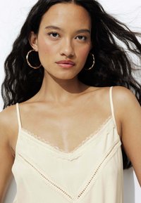 Camisole beige clair avec bordure en dentelle et fines bretelles. Présente un décolleté en V délicat et des détails en dentelle élaborés le long du bustier.