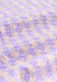 Lättviktig vävt tyg med ett lila och beige rutmönster, med en mjuk textur och en något skrynklig yta.