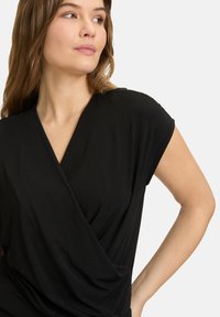 Zwarte wikkeltop met korte mouwen, zachte stof, V-halslijn en gedrapeerd ontwerp aan de voorkant, wat zorgt voor een relaxte pasvorm.