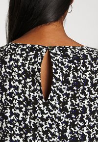 Haut en tissu à motifs noir et blanc avec une petite ouverture en forme de clé à l'arrière, fermée par un bouton rond. Texture douce.