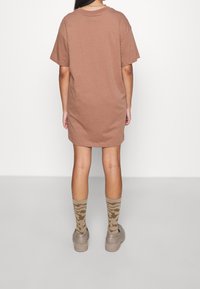 Brąsowa, luźna sukienka T-shirtowa, krótki rękaw, zaokrąglony dół. Poł�ączona z wzorzystymi skarpetkami i masywnymi beżowymi sneakersami. Gładka bawełniana tekstura.