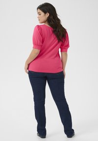 Haut rose à manches courtes avec des manches bouffantes, associé à un jean droit bleu foncé. Tissu lisse et design ajusté.