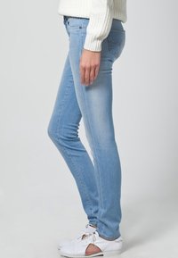 Light blue skinny jeans made from denim, featuring a smooth texture and subtle fading. Styled with white casual shoes.