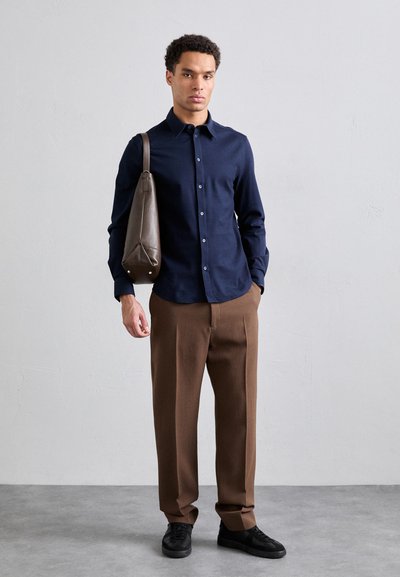 Camisa de botones navy, pantalones tállate marrones, zapatillas negras y un bolso de hombro de cuero marrón con bordes redondeados. Diseño simple y limpio.