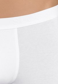 Weiße Boxershorts aus weichem Stoff mit einem breiten elastischen Bund, der mit "SLOGGI" geprägt ist, und einer glatten Oberfläche.