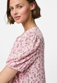 Růžová květinová blůza s texturovanou tkaninou, nabíranými rukávy a nařaseným výstřihem, na kterém jsou malé, jemné květiny s zelenými akcenty.