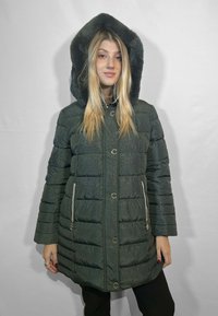 Giacca imbottita di un verde scuro con un ampio cappuccio foderato in pelliccia, chiusure con bottoni metallici e tasche laterali. Tessuto strutturato con una lieve lucentezza.