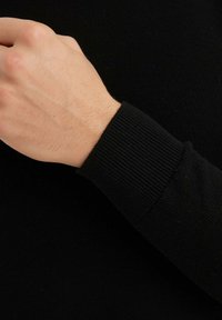 Poignet de pull en tricot noir avec une texture côtelée. Le tissu semble doux et extensible, avec un ajustement près du poignet.