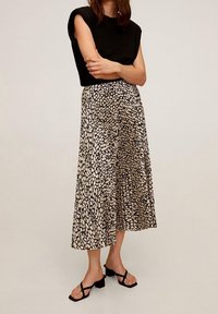 Top corto nero a maniche corte abbinato a una lunga gonna beige e nera con un motivo, caratterizzata da un design fluido e una leggera lucentezza. Sandali neri completano il look.