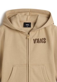 Beige hoodie med dragkedja framtill, kängurufickor och en brun "VANS"-logotyp tryckt på bröstet. Mjuk, texturerad fleece-tyg.