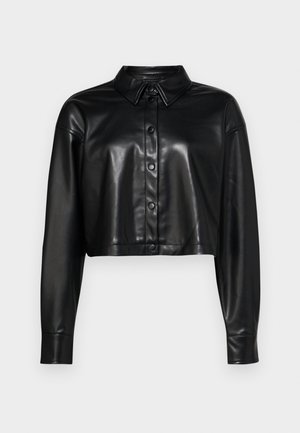 Supjaustyta juodos odos marškiniai su sagomis priekyje, smailiu apykakle ir ilgomis rankovėmis. Yra blizgus paviršius ir standartinės sagų detalės.