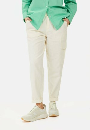 Beige cargobroek met een ontspannen pasvorm, voorzien van zijzakken en opgerolde manchetten. Gecombineerd met lichtgrijze sneakers met textuuraccenten.