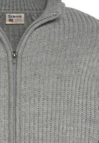 Szary dzianinowy sweter z zamkiem błyskawicznym, z prążkowanym wykończeniem, z wysokim kołnierzem i srebrnym zapięciem. Etykieta widoczna wewnątrz kołnierza.