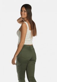 Crop top blanc à rayures avec bretelles larges, associé à un pantalon cargo taille haute vert olive, doté de poches latérales et d'une coupe slim.