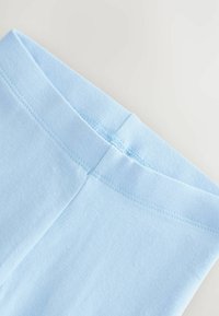 Hellblaue Stoffleggings mit elastischem Bund und Flatlock-Nahtdetail auf neutralem Hintergrund.