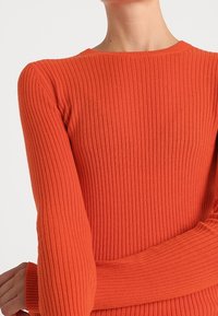 Ribbad orange tröja med rundad halsringning, figurnära långa ärmar och ett strukturerat, stretchigt material.