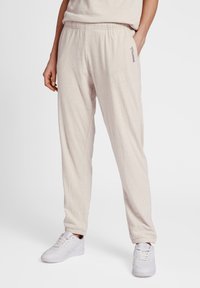 Light beige jogger pants made of soft fabric, featuring an elastic waistband, cuffed hems, and a subtle brand logo on the side.
