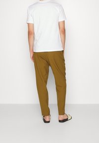 T-shirt blanc à manches courtes, pantalon marron et sandales noires avec des accents crème. Le pantalon a une coupe décontractée et des jambes effilées.