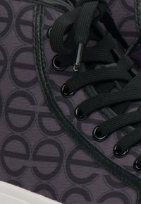 Czarne sneakersy z fakturowanym materiałem o powtarzającym się okrągłym wzorze, czarnymi sznurowadłami i okrągłymi oczkami. Akcent w postaci białej gumowej podeszwy.