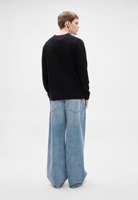 Camisola preta com decote redondo, apresentando mangas compridas. Combinada com calças de ganga azul clara de perna larga, exibindo um corte descontraído e tecido texturizado.