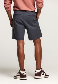 Shorts bleu marine en coton, avec des poches arrière et une coupe droite. Associés à des baskets montantes blanches et bordeaux.
