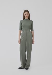 Lys grøn ribbet turtleneck-top parret med høj talje, vide bukser i matchende stof og farve; glat tekstur, minimale accenter.