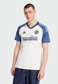 Weißes Sporttrikot mit blauen Akzenten, V-Ausschnitt, kurzen Ärmeln, mit "NASHVILLE"-Logo auf der Vorderseite und drei Streifen-Design auf den Schultern.