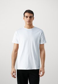 T-shirt blanc à col rond en coton, avec des manches courtes et un petit logo discret au niveau de l'ourlet. Texture lisse et coupe regular.