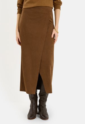 Falda midi marrón ajustada combinada con botines de cuero marrón oscuro hasta la mitad de la pantorrilla y pulsera dorada en la muñeca izquierda, llevada por una persona de pie.