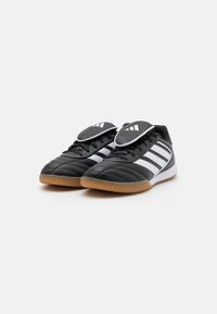Black leather sports shoes with three white stripes, rubber gum sole, padded tongue, and stitched design. Lightweight with a low profile.