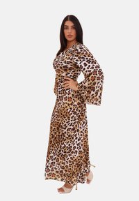 Abito lungo con stampa leopardata e maniche lunghe a campana; presenta sfumature di marrone, beige e nero su uno sfondo bianco; texture liscia.