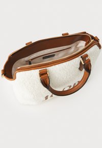 Hvid faux shearling taske med brune læderhåndtag og -detaljer, lynlåslukning og en lysefarvet inderside med lomme.