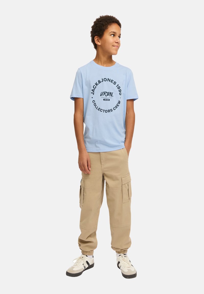 Camiseta de algodón azul claro con texto de logo circular negro; combinada con pantalones cargo beige y zapatillas blancas con acentos negros.