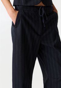 Pantalon bleu marine à fines rayures, en tissu lisse, doté d'une taille élastique avec un cordon de serrage et de poches latérales.