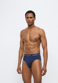 Σκούρα μπλε εσώρουχα με στενή εφαρμογή, από μαλακό ύφασμα, με ελαστική μέση που φέρει την επιγραφή "Calvin Klein" και κλασικό σχεδιασμό κόμματος.