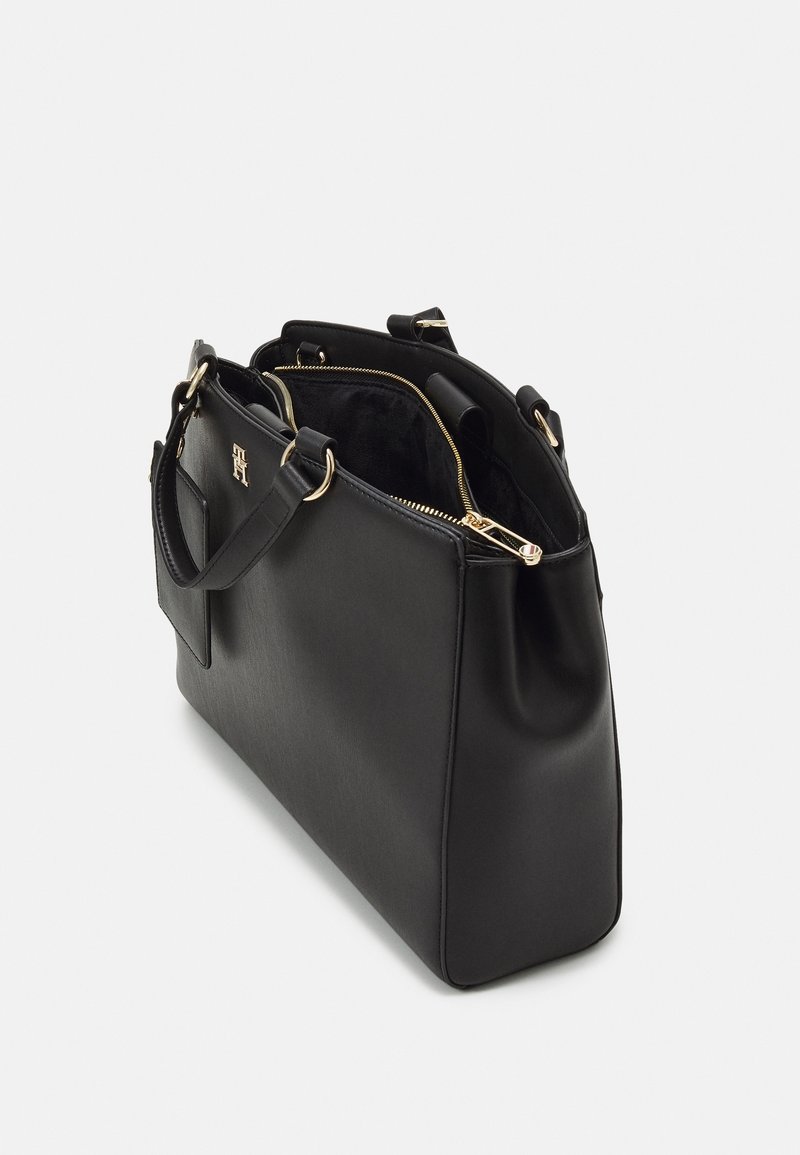 Sac à main en cuir noir avec fermeture éclair dorée partiellement ouverte, doubles poignées et petite poche extérieure sur fond blanc uni.