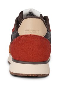 WODEN brand sneaker featuring a brown mesh upper, red suede accents, beige heel section, textured rubber sole, and contrasting stitching.