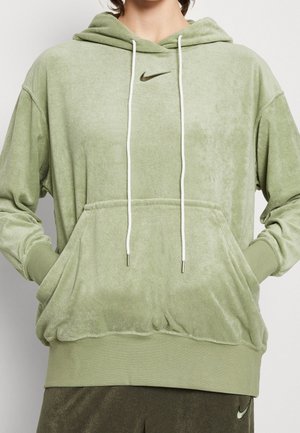 Hellgrüner Nike Kapuzenpullover mit weißen Kordeln und Fronttasche, getragen von einer Person mit den Händen in der Tasche.