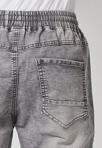 Šedé džínové joggers s elastickým pasem, obsahující zadní kapsu. Látka má vybledlý, texturovaný vzhled s kontrastním prošíváním.