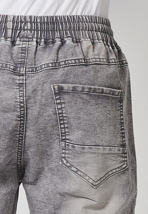 Sive traperice s elastičnim pojasom, koje imaju stražnji džep. Tkanina ima izblijedjeli, teksturirani izgled s kontrastnim šavovima.