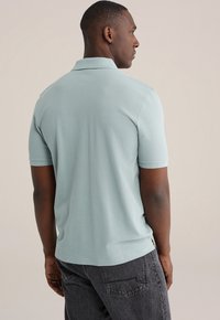 Lichtblauw poloshirt met korte mouwen gemaakt van katoen, met een klassieke kraag en nette stiksels, gecombineerd met donkergrijze spijkerbroek.