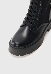 Botte de combat en cuir noir avec semelle à forte traction, lacets noirs et panneaux latéraux texturés avec un motif subtil.