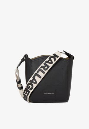 Black leather crossbody bag with a structured shape. Features a contrasting cream strap displaying "KARL LAGERFELD" in black lettering.