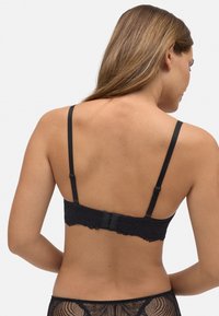 Bralette de encaje negro con tirantes ajustables, bordes con forma de ola y cierre de gancho en la parte posterior. Tejido suave con detalles de patrón intrincado.