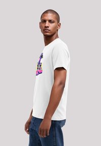 White cotton t-shirt with a colorful graphic print featuring a figure. Short sleeves, round neckline, and casual fit. Denim jeans visible.