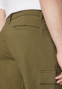 Olivgrüne Cargo-Hosen aus strukturiertem Stoff, mit einem Design für eine Gesäßtasche und Gürtelschlaufen, sowie flachen Nähten für Langlebigkeit.