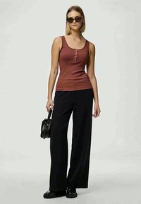Rustfarvet ribbet tanktop med knappedetalje, kombineret med løstsiddende sorte bukser og sorte sko, komplet med solbriller og en lille taske.