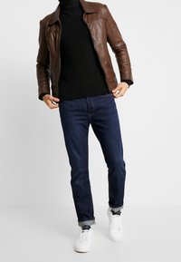 Brun läderjacka, svart rullkrage tröja, blå jeans och vita sneakers. Klassisk passform med uppvikta ärmar och en slät textur.