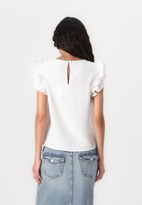 Hvit topp med volanger på ermene og en spalte bak, kombinert med et blått denimskjørt med to baklommer.